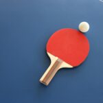 Ein roter Tischtennisschläger mit weißem Ball auf einer blauen Platte. Foto von Lisa Keffer auf Unsplash