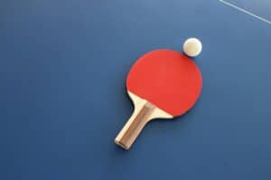 Ein roter Tischtennisschläger mit weißem Ball auf einer blauen Platte. Foto von Lisa Keffer auf Unsplash